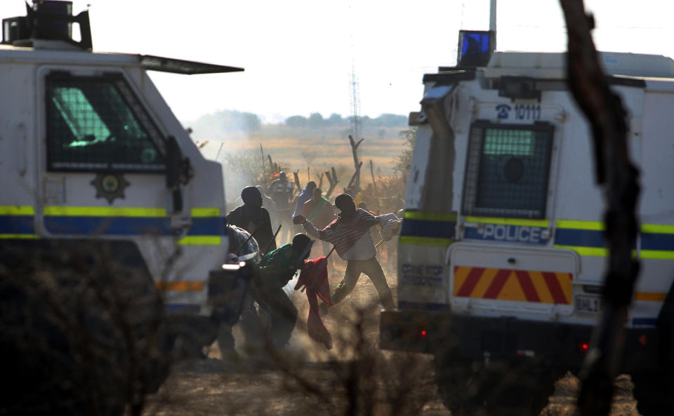 Striking mineworkers throw stones as police open fire on striking miners at the Lonmin Platinum Mine near Rustenburg, South Africa, Thursday, Aug. 16, 2012. South African police opened fire Thursday on a crowd of striking workers at a platinum mine, leaving an unknown number of people injured and possibly dead. Motionless bodies lay on the ground in pools of blood. (AP Photo)