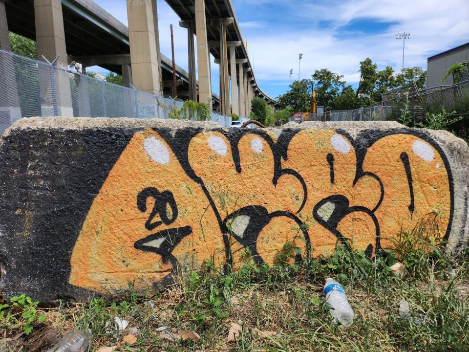 <p>A picture taken with the Galaxy Z Flip 4 showing a wall with orange graffiti spray painted on it, with a highway and some trees in the background.</p>
