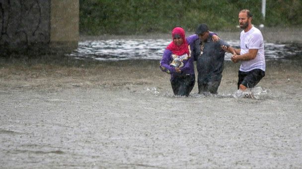 PHOTO: A man helps two people walk through flood water after their car got stuck in St. Louis, Mo., July 28, 2022. (Allie Schallert/AP)