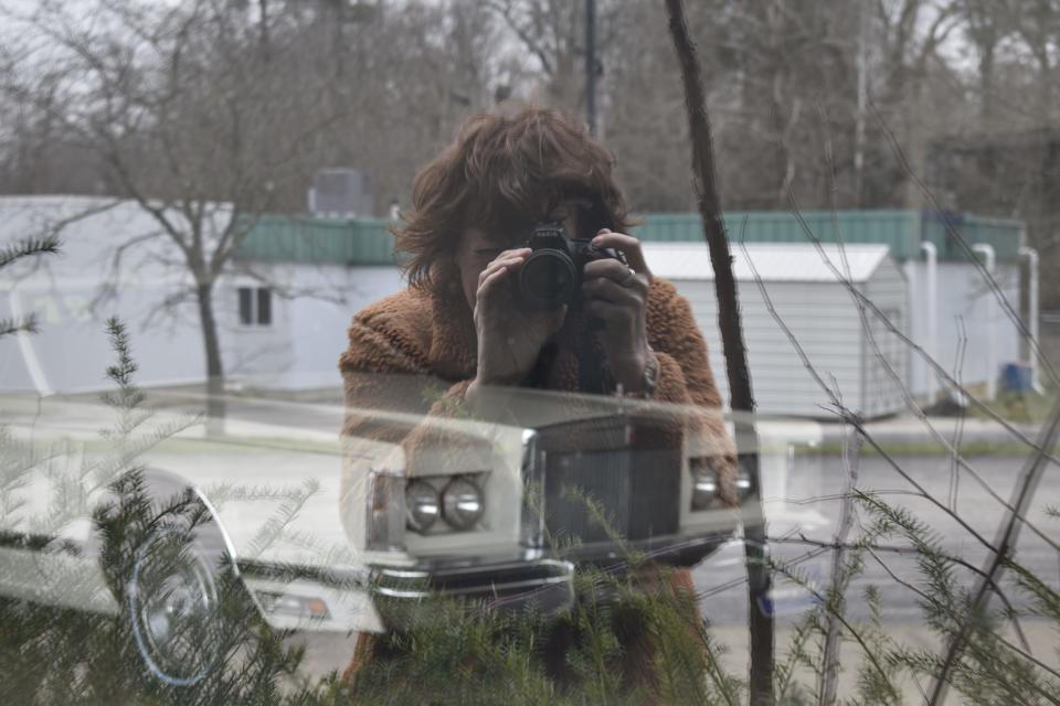 My Favorite Ride columnist Laura Lane is reflected in a window Friday while attempting to get a more close-up photo of a 1978 Lincoln Continental in plain-view storage at an old car lot showroom.