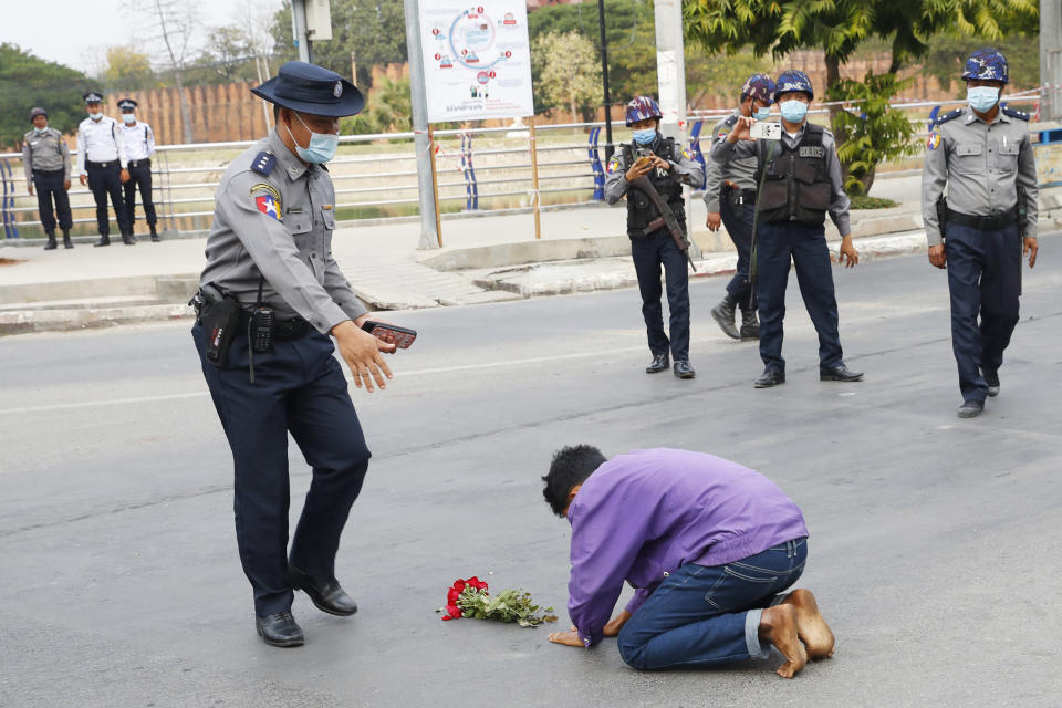 A protest supporter offers flowers and kneels on a road before a police officer in Mandalay, Myanmar, on Feb. 6, 2021. Protests in Myanmar against the military coup that removed Aung San Suu Kyi’s government from power have grown in recent days despite official efforts to make organizing them difficult or even illegal. (AP Photo)