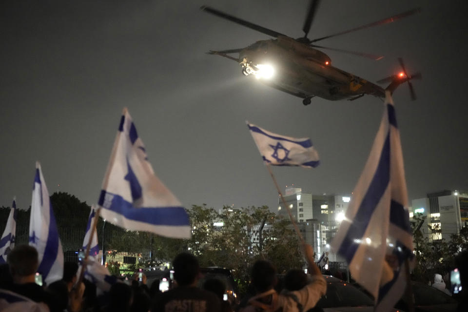 Varias personas ondean banderas israelíes bajo un helicóptero que traslada a rehenes liberados por Hamás en Gaza a su llegada al helipuerto del hospital infantil Schneider, en Petah Tikva, Israel, el 26 de noviembre de 2023. (AP Foto/Leo Correa)