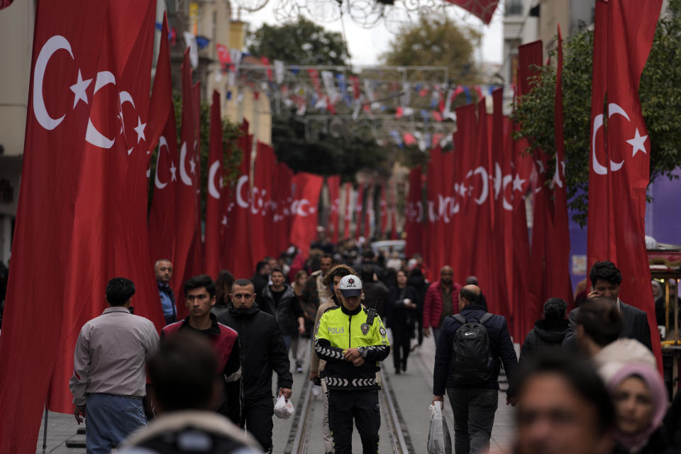 A police officer stands as other people walk in the decorated with Turkish flags Istanbul's popular pedestrian Istiklal Avenue in Istanbul, Monday, Nov. 14, 2022. Turkish police said Monday that they have detained a Syrian woman with suspected links to Kurdish militants and that she confessed to planting a bomb that exploded on a bustling pedestrian avenue in Istanbul, killing six people and wounding several dozen others.(AP Photo/Khalil Hamra)
