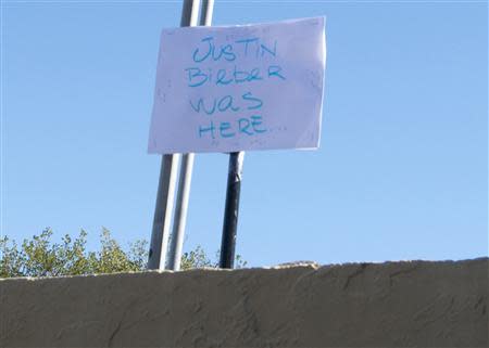 A sign reading "Justin Bieber was here" stands along a wall on the inside of a police lot where pop singer Justin Bieber's rented yellow Lamborghini sports car was impounded in Miami Beach, Florida January 23, 2014. REUTERS/Gary I. Rothstein