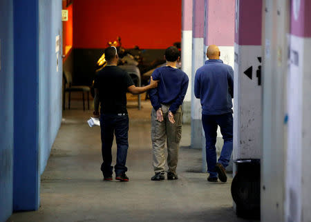 U.S.-Israeli teen (C) arrested in Israel on suspicion of making bomb threats against Jewish community centres in the United States, Australia and New Zealand over the past three month, is escorted by security personnel following his remand hearing at Magistrate's Court in Rishon Lezion, Israel March 23, 2017. REUTERS/Baz Ratner