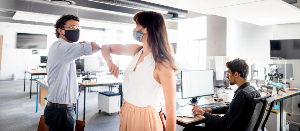 Young people working in an office, wearing masks and greeting each other with an elbow touch..