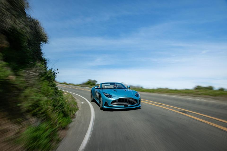 a blue aston martin db12 volante driving down a road