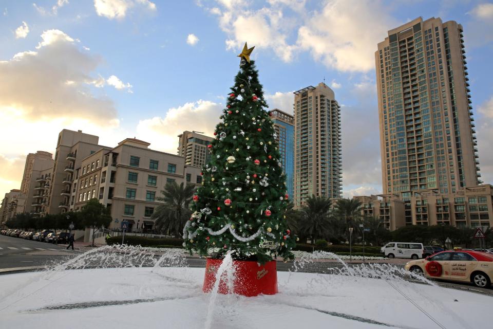 In this Saturday, Dec. 21, 2013 photo, a large Christmas tree with fake snow around it, is showcased on a street in Dubai, United Arab Emirates. The Middle East’s brashest city is increasingly embracing the trappings of Christmas in a way that would be unthinkable in more conservative parts of the Muslim world. Christmas trees adorn shopping centers and residential neighborhoods, and high-end hotels try to outdo one another with extravagant and boozy holiday dinners. (AP Photo/Kamran Jebreili)