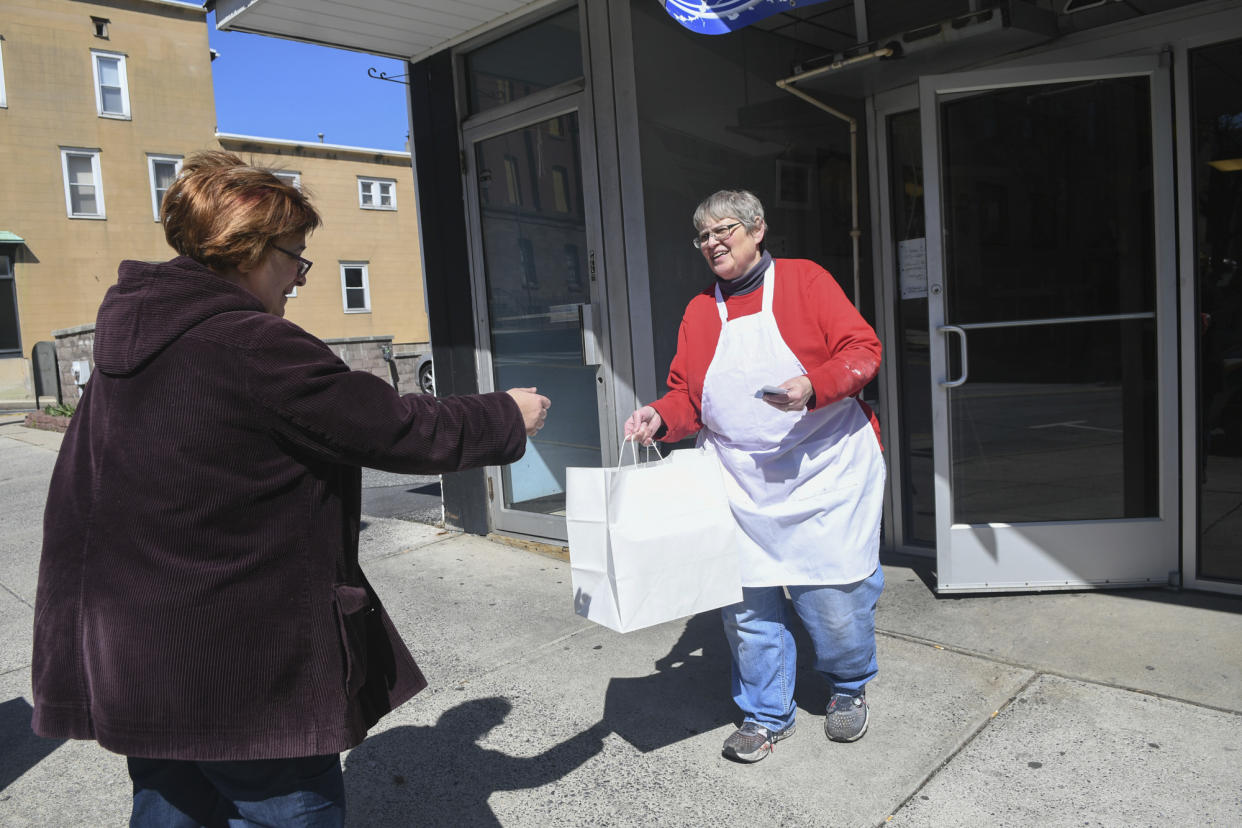 Mildred A. Kennedy, owner of Momma Millie's Bakery, hands Christine Romanko, her blueberry pie, Jewish apple cake and sticky buns order in front of her bakery in Pottsville, Pa., on March 21, 2020. (Jacqueline Dormer/The Republican-Herald via AP)
