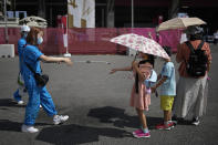 A volunteer sprays water on children as they use umbrellas to beat the heat outside the Fuji International Speedway, the finish for the women's cycling road race that is underway, at the 2020 Summer Olympics, Sunday, July 25, 2021, in Oyama, Japan. (AP Photo/Christophe Ena)