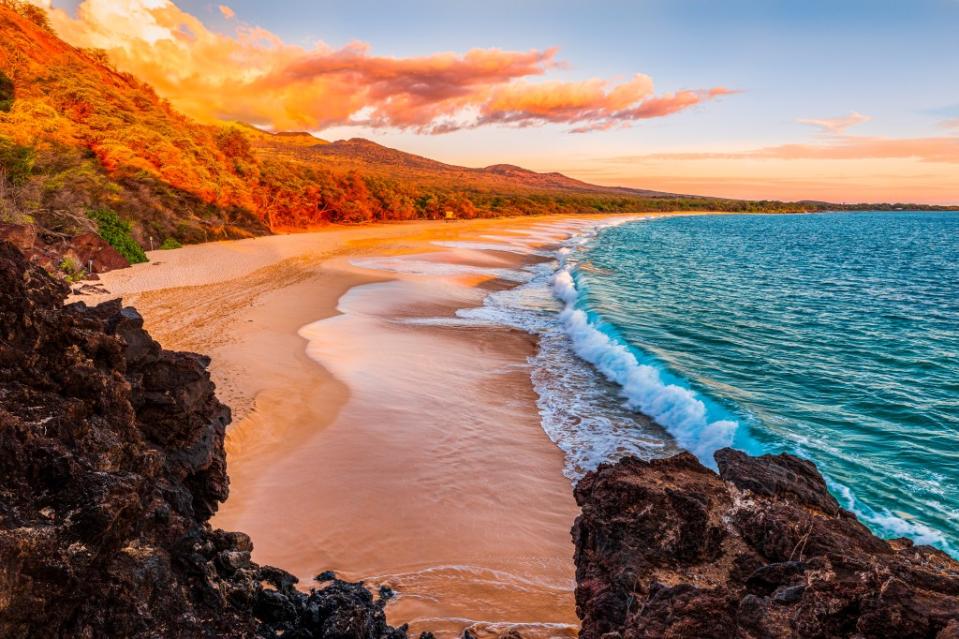 A large wave crashes on the beach at sunrise at Makena Beach, Maui, Hawaii via Getty Images