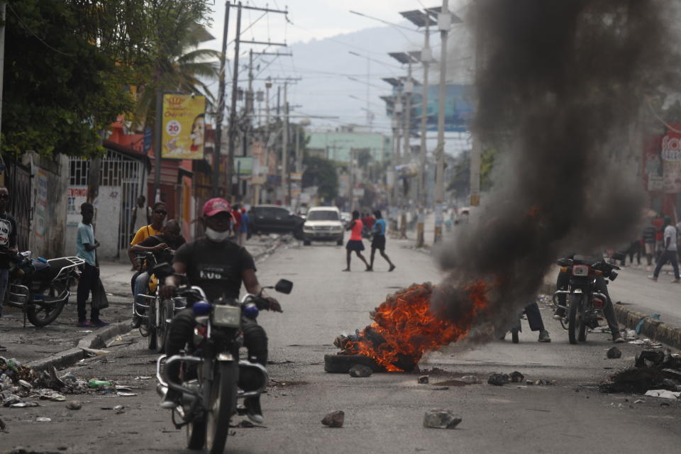 A motocyclist rides past a burning barricade set up by protesters in Port-au-Prince, Haiti, Monday, Sept. 30, 2019. Opposition leaders are calling for a nationwide push Monday to block streets and paralyze Haiti's economy as they press for Moise to give up power, and tens of thousands of their young supporters were expected to heed the call. (AP Photo/Rebecca Blackwell)