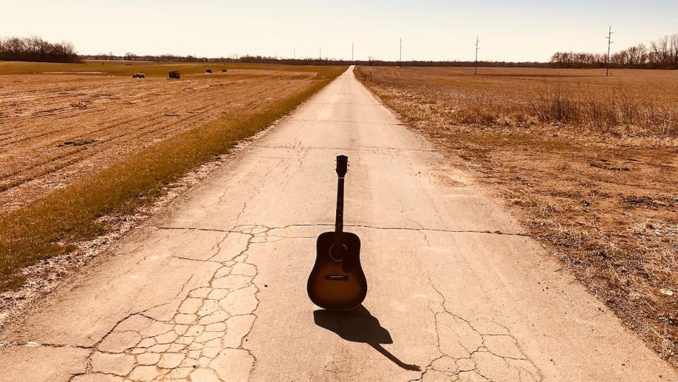 A lone acoustic guitar sits in the middle of an old deserted road out in themiddle of nowhere during the day