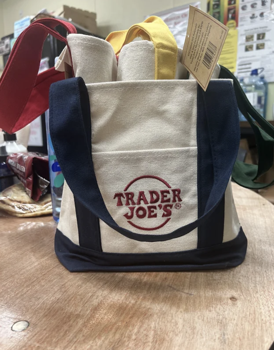 Trader Joe's branded canvas grocery bags with various colored handles displayed on a counter