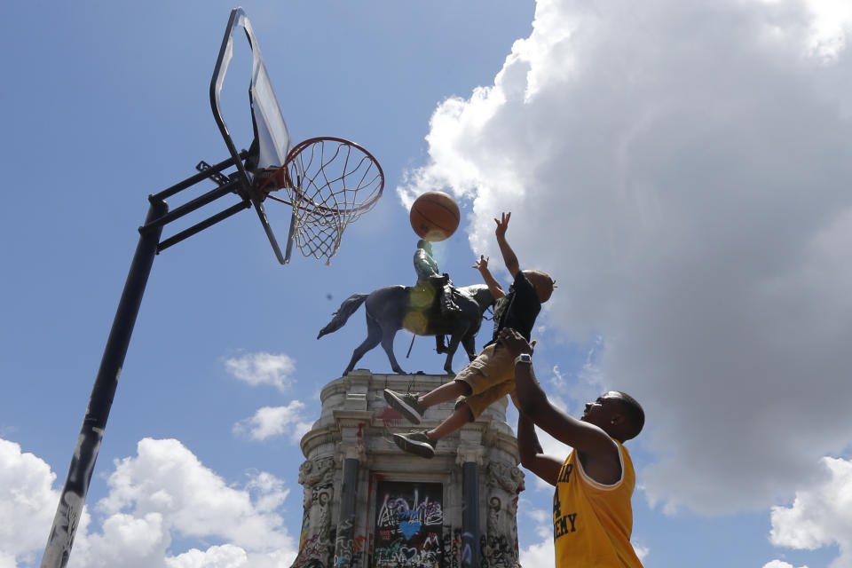 Garth Bowen, lifts his son, Elijah so he can take a shot at a basketball hoop in front of the statue of Confederate General Robert E. Lee on Monument Avenue Sunday, June 21, 2020, in Richmond, Va. A judge extended an injunction delaying the removal of the statue by the state. The statue had become a focal point for the Black Lives Matter movement in Richmond. (AP Photo/Steve Helber)