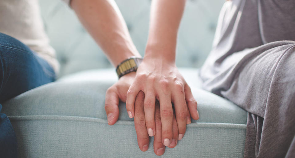 A couple on a sofa with the woman's hand on top of man's hand.