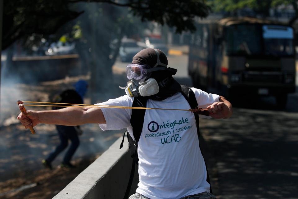 Un manifestante antigubernamental enmascarado usa un tirador para arrojar canicas contra la Guardia Nacional Bolivariana durante enfrentamientos en Caracas, Venezuela, el sábado 22 de marzo de 2014. (Foto AP/Fernando Llano)