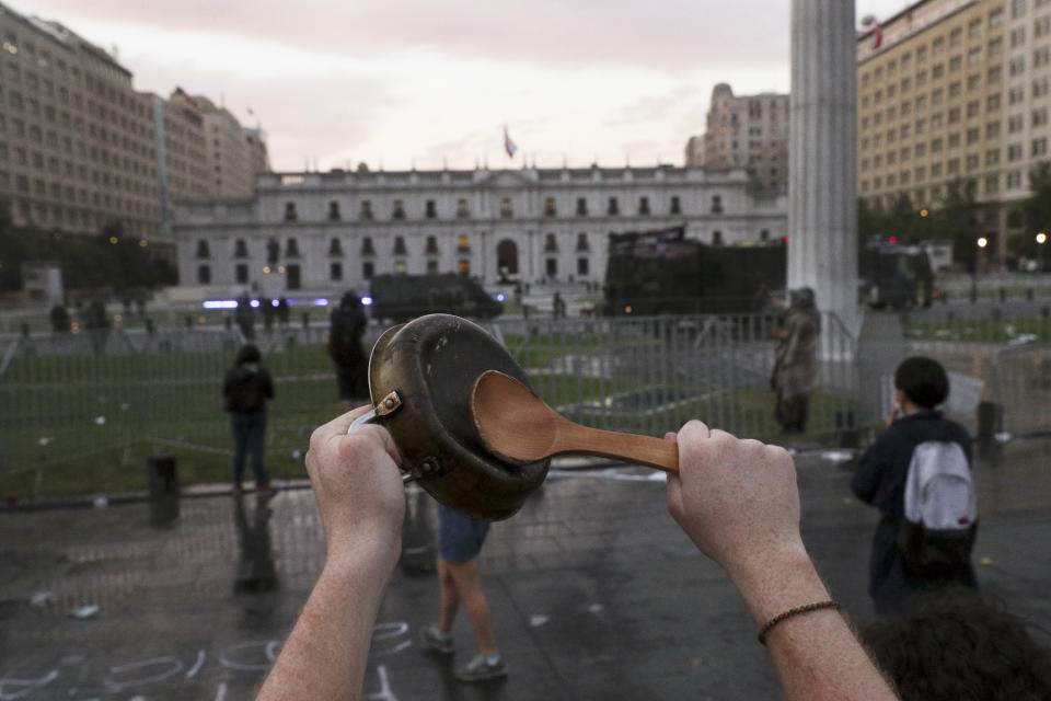 An anti-government protester bangs on a pan in front of La Moneda presidential palace in Santiago, Chile, Friday, Oct. 25, 2019. A new round of clashes broke out Friday as demonstrators returned to the streets, dissatisfied with economic concessions announced by the government in a bid to curb a week of deadly violence.(AP Photo/Esteban Felix)