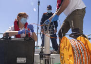 In this picture taken on Thursday, May 21, 2020, Italian Lazio region's environmental agency biologists Salvatore De Bonis, right, and Valentina Amorosi show how they perform tests on sea water during an interview with The Associated Press on a Coast Guard boat off Fiumicino, near Rome. Preliminary results from a survey of seawater quality during Italy’s coronavirus lockdown indicate a sharp reduction in pollution from human and livestock waste in the seas off Rome. Authorities stressed it was too soon to give the lockdown sole credit for the change. (AP Photo/Domenico Stinellis)