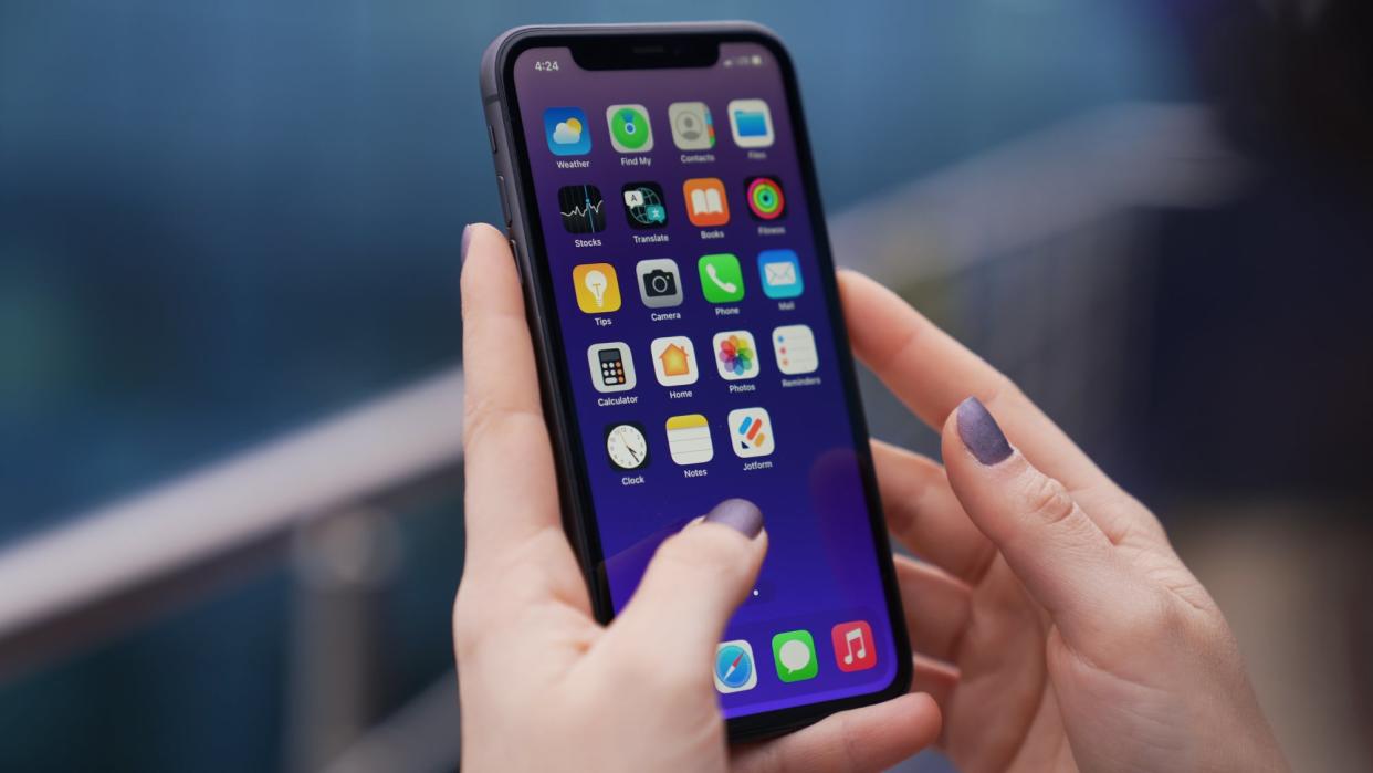 A woman holding an unlocked iPhone with a number of apps on the screen, including the Find My app.