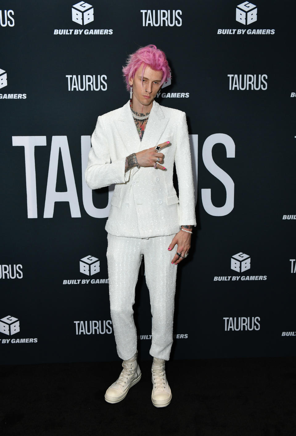 MGK pulling a "rock n roll" finger sign in a suit at the premiere of "Taurus"