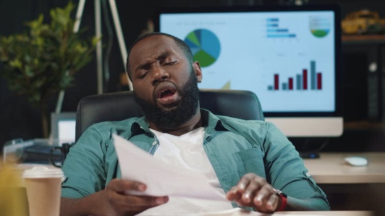 Man reclines with eyes closed, holding paperwork