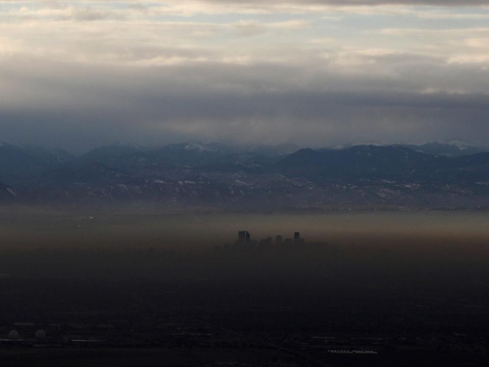 tall buildings poke out above layer of green brown smog in valley with mountains in the background