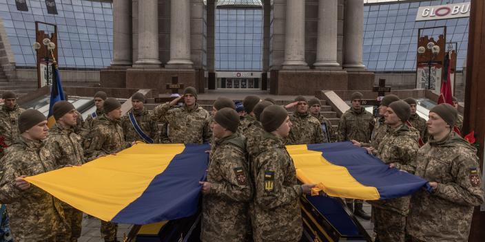 soldiers carrying caskets draped in Ukrainian blue and yellow flags