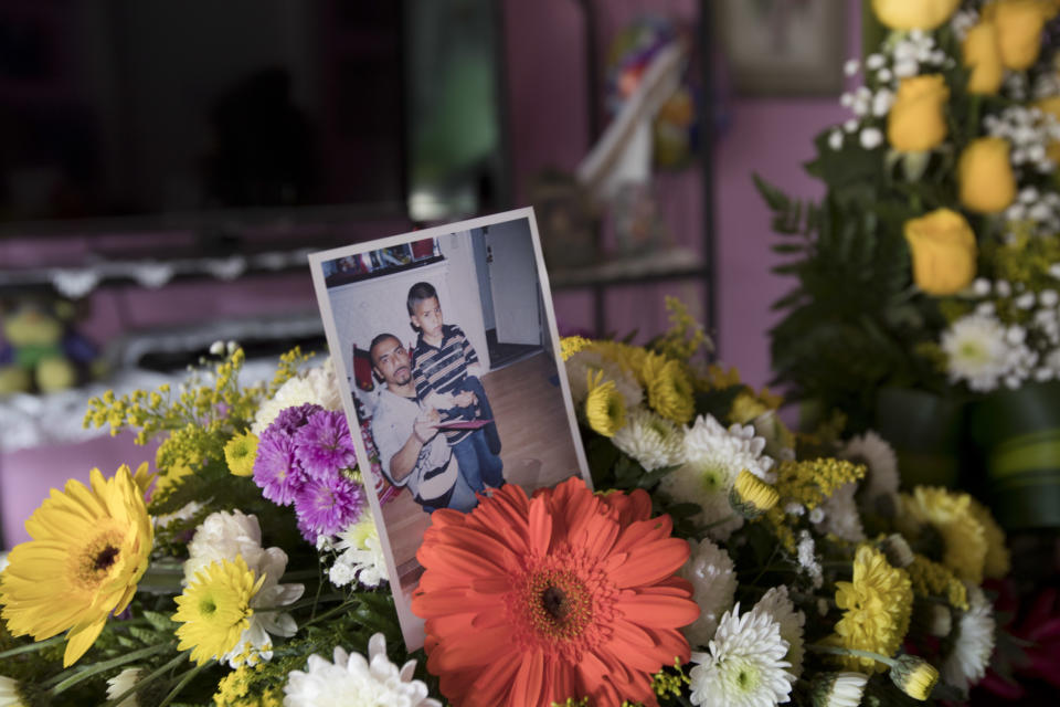 This Oct. 31, 2018 photo shows a family photo of Wilmer Gerardo Nunez with his younger brother Mynor placed in a bouquet of flowers adorning the coffin that contains the remains of Wilmer during a wake at his mother's home in Ciudad Planeta neighborhood of San Pedro Sula, Honduras. Nunez' children in Los Angeles still don't know their father is dead. (AP Photo/Moises Castillo)