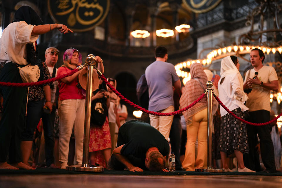 A Muslim worshipper, center, prays out of the praying time as tourists visit Byzantine-era Hagia Sophia mosque in Istanbul, Turkey, Tuesday, July 4, 2023. With tourism reaching or surpassing pre-pandemic levels across Southern Europe this summer, iconic sacred sites struggle to find ways to accommodate both the faithful who come to pray and millions of increasingly secular visitors attracted by art and architecture. (AP Photo/Francisco Seco)