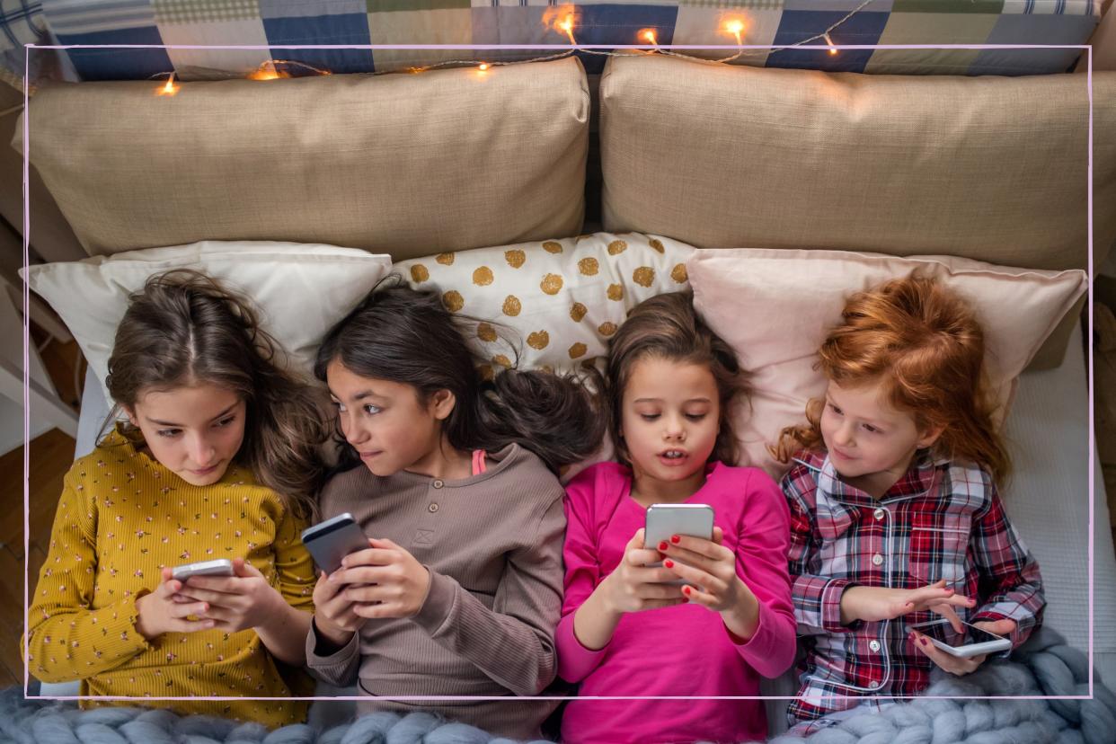  Four young girls lying in bed while looking at their smartphones. 