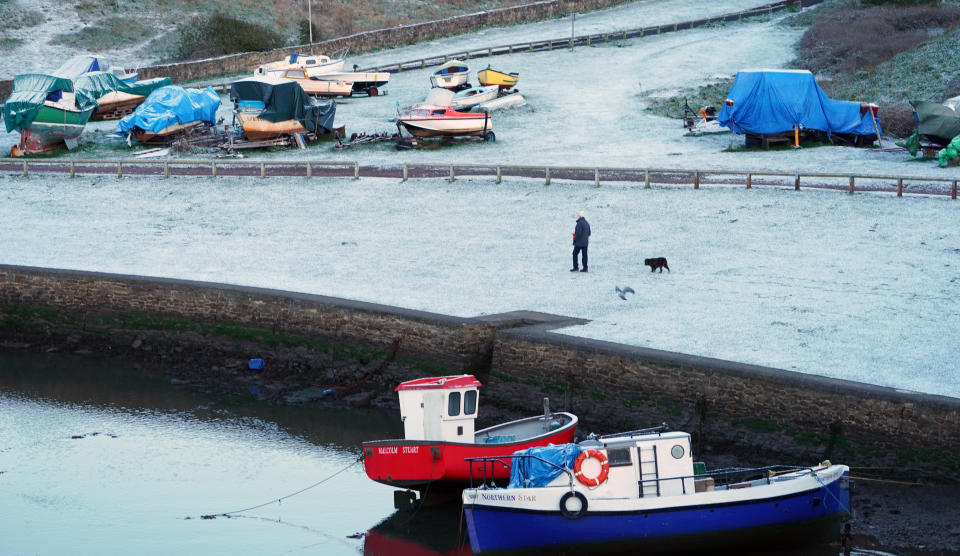 A man walks a dog in a light dusting of overnight snow at Seaton Sluice on the North East coast. Picture date: Sunday April 11, 2021.