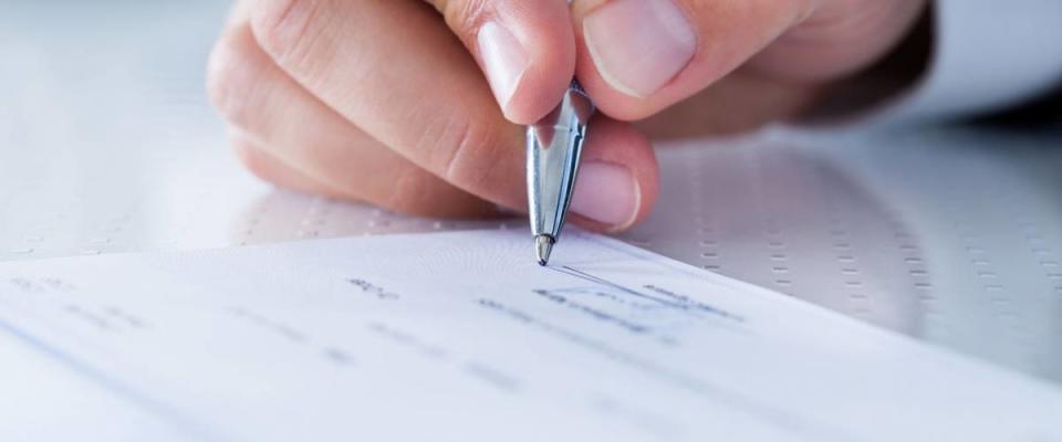 A Male Hand Filling Out The Amount On A Cheque