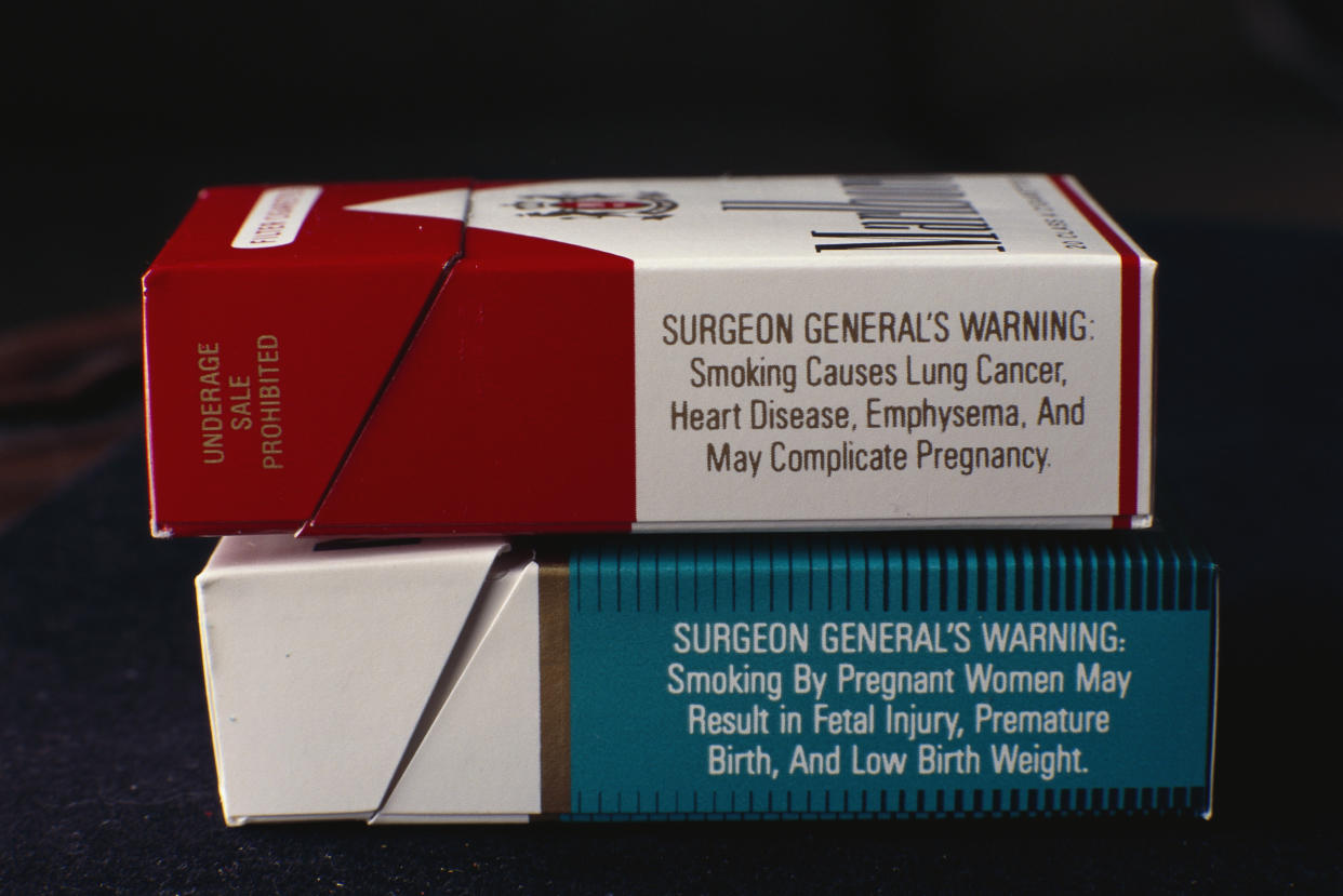 Two stacked boxes of cigarette, Marlboro on top, Newport on bottom, showing surgeon general's warning labels on the side of their packages.