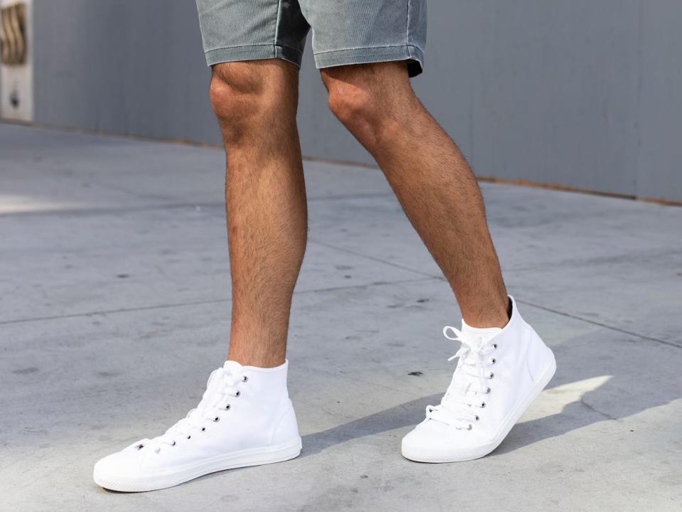 lower half of a man's body walking on the street wearing gray shorts and white high top sneakers