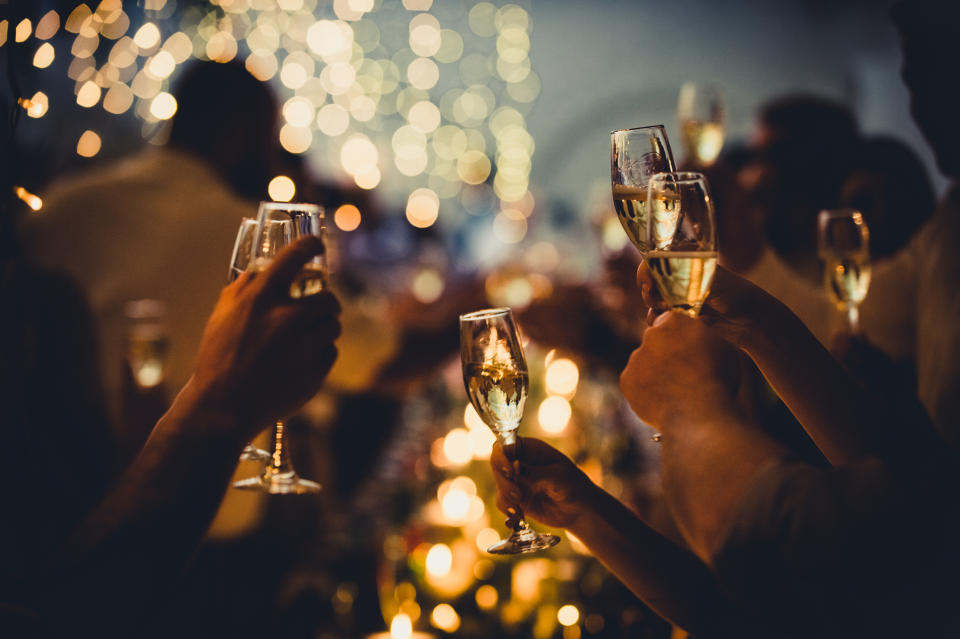 Guests raise champagne glasses in a toast at a wedding reception, with blurred lights and decorations in the background