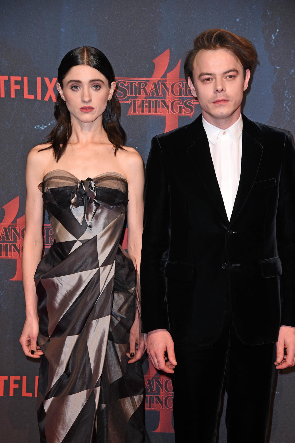 Two actors at a 'Stranger Things' event, woman in a strapless dress with bow detail, man in black velvet suit