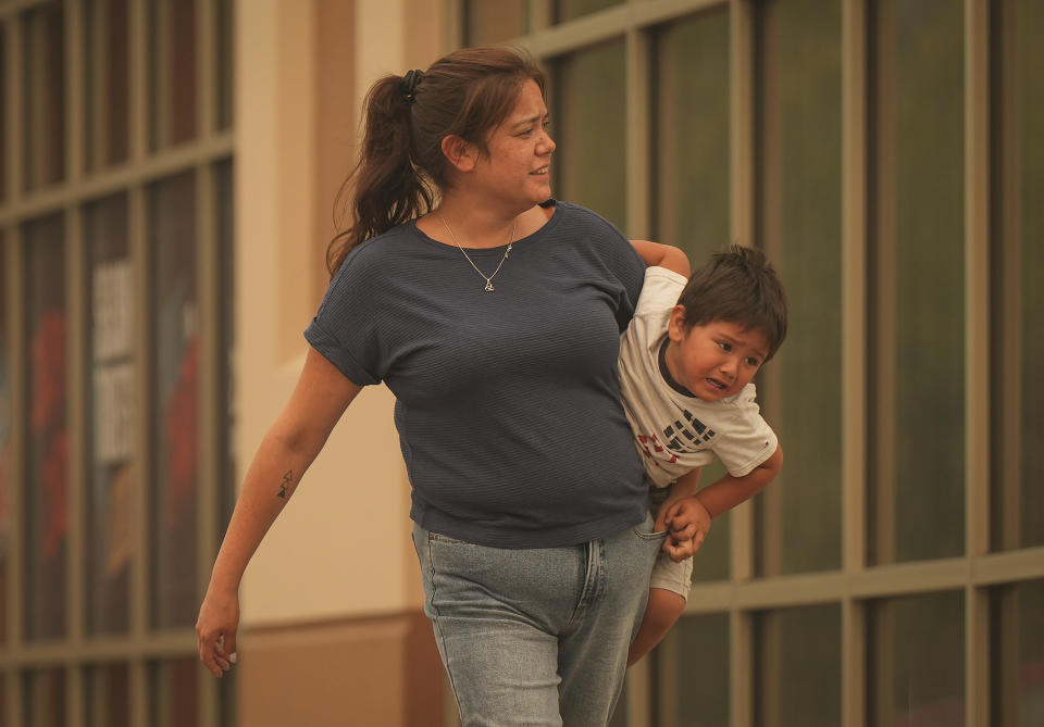 A woman carries a young boy outside an evacuation center for those forced from their homes due to wildfires, in Kelowna, British Columbia, Saturday, Aug. 19, 2023. (Darryl Dyck/The Canadian Press via AP)