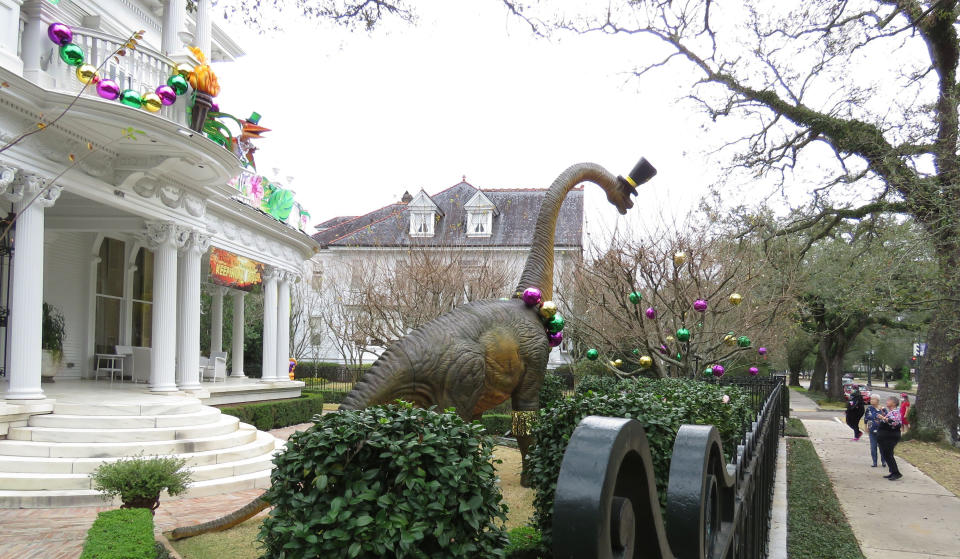 Passersby look at dinosaurs on the balcony of a mansion on St. Charles Avenue in New Orleans, Tuesday, Jan. 26, 2021. The banner says "Thank you, Mayor, for keeping us safe." Because pandemic dangers from large and widespread crowds have canceled Mardi Gras parades in New Orleans this year, thousands of people are decorating their homes as floats. (AP Photo/Janet McConnaughey)