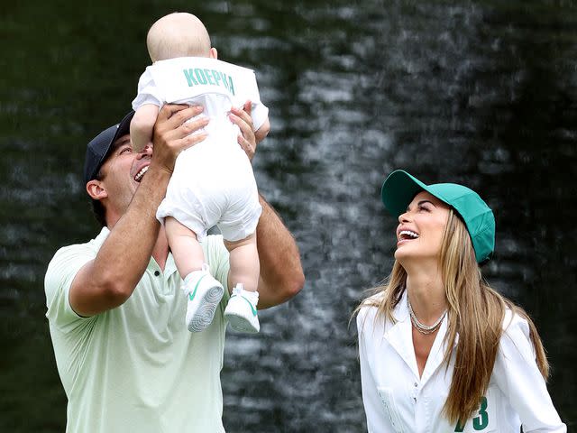 <p>Warren Little/Getty</p> Brooks Koepka holds his son, Crew, with Jena Sims on the ninth green during the Par Three Contest prior to the 2024 Masters Tournament on April 10, 2024.