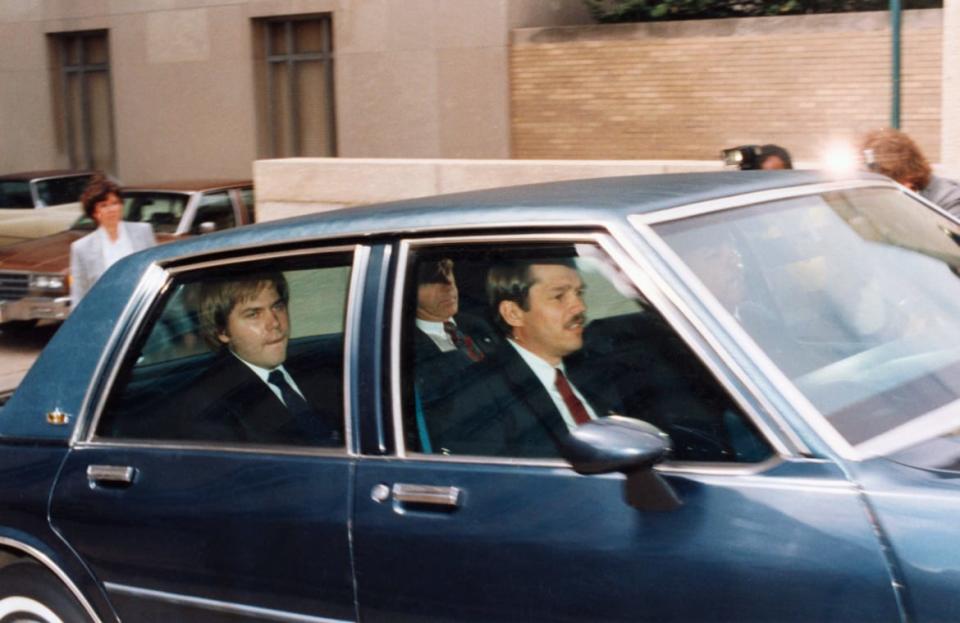 John Hinckley, Jr., accused of attempting to assassinate President Reagan, sits in the back of an official vehicle outside D.C. federal court.