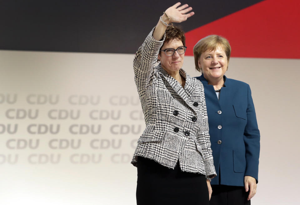 Newly elected CDU chairwoman Annegret Kramp-Karrenbauer, left, is flanked by German Chancellor Angela Merkel, right, as she waves during the party convention of the Christian Democratic Party CDU in Hamburg, Germany, Friday, Dec. 7, 2018, after German Chancellor Angela Merkel didn't run again for party chairmanship after more than 18 years at the helm of the party. (AP Photo/Michael Sohn)