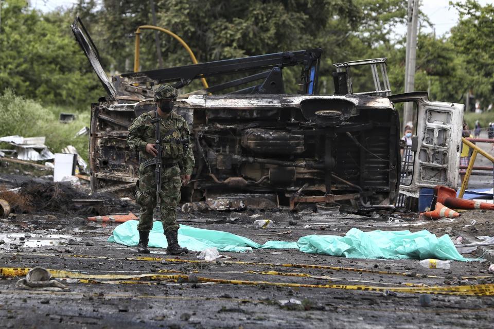 A soldier stands guard in front of the charred remains of a car that was burned by protesters during a night of clashes with police in Yumbo, near Cali, Colombia, Tuesday, May 18, 2021. Colombians have taken to the streets for weeks across the country after the government proposed tax increases on public services, fuel, wages and pensions, but have continued even after President Ivan Duque walked back the tax hike. (AP Photo/Andres Gonzalez)