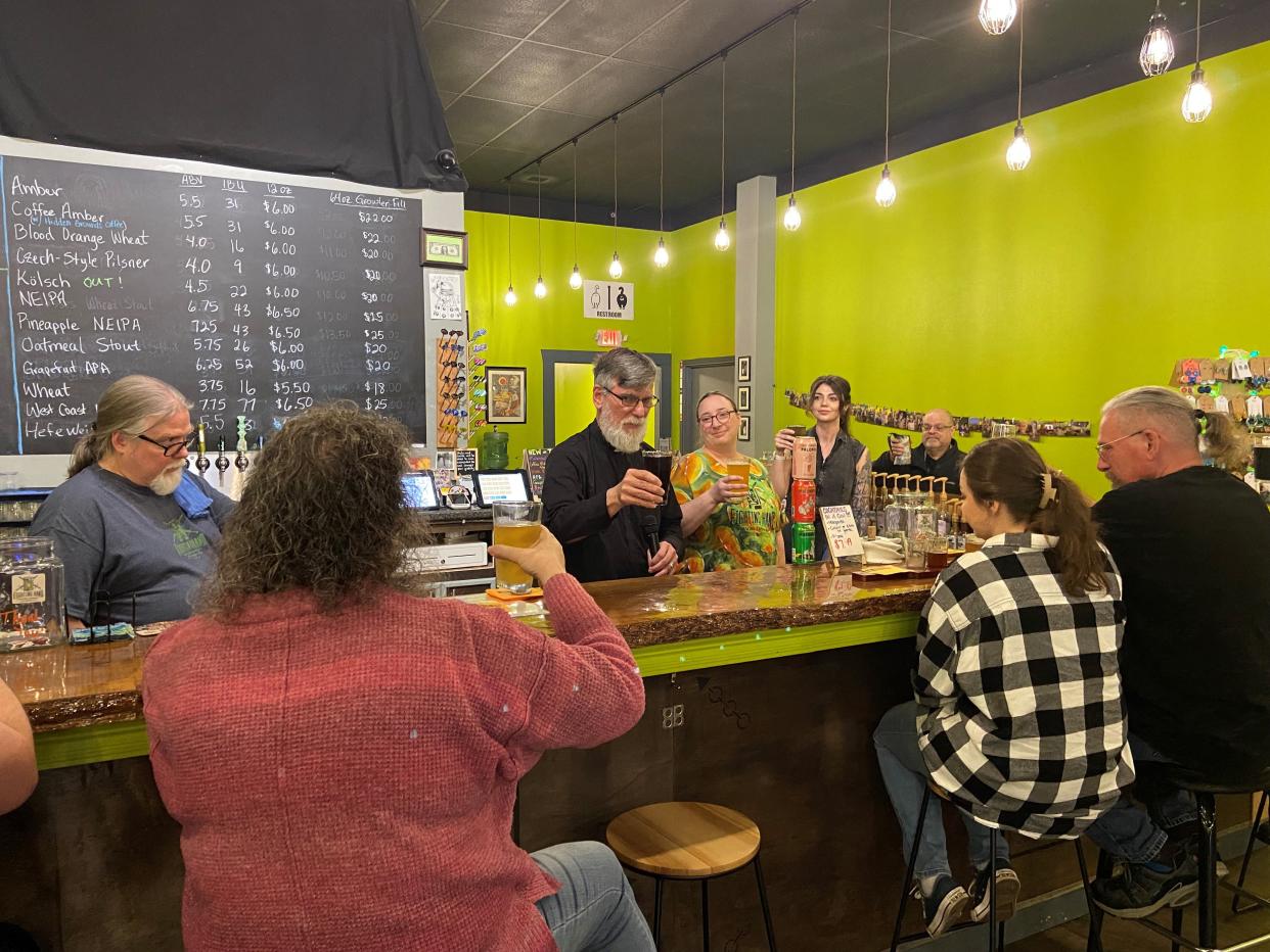Father Steve Brandow (center) stands between owners Chris and Tiffany Lindsey behind the bar at the Fighting Hand Brewing Company in Pineville as he blesses their beers on Saturday, the day before St. Patrick's Day.