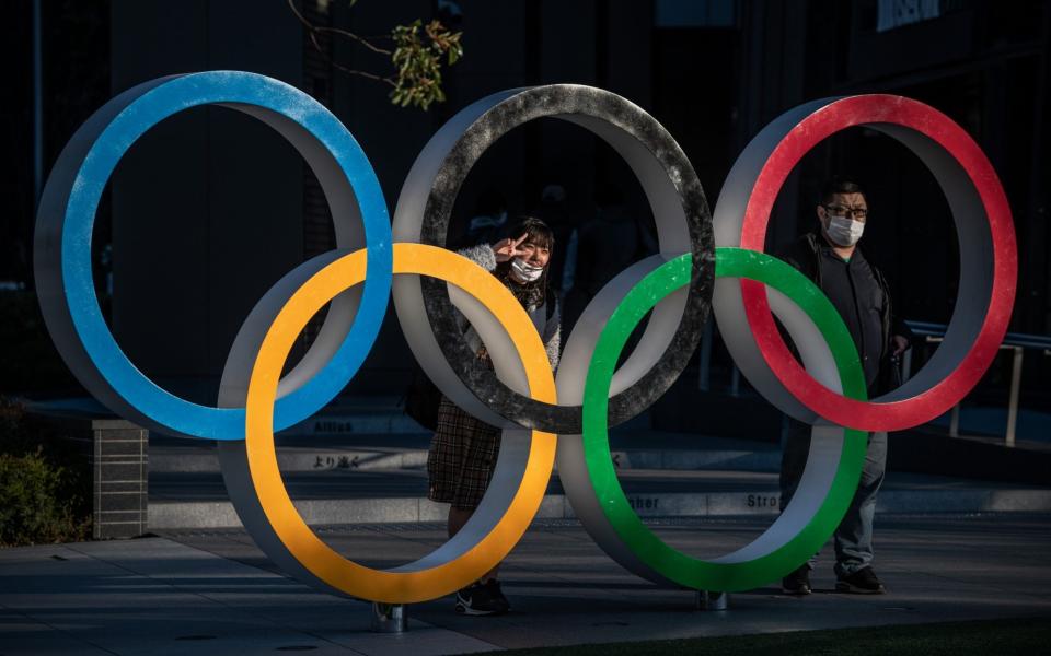 People wearing face masks pose for photographs next to Olympic Rings  - Getty Images