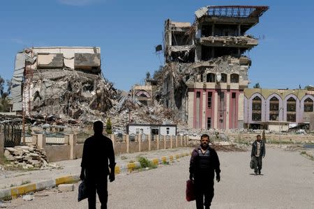 People walk in front of the remains of the University of Mosul, which was burned and destroyed during a battle with Islamic State militants, in Mosul, Iraq, April 10, 2017. REUTERS/Marko Djurica/Files