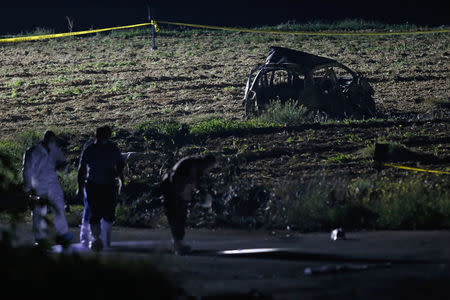 Forensic experts use lights as they look for evidence on a road near a field after a powerful bomb blew up a car (Rear) and killed investigative journalist Daphne Caruana Galizia in Bidnija, Malta, October 16, 2017. REUTERS/Darrin Zammit Lupi