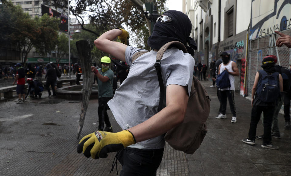 A demonstrator throws stones at police during an anti-government protest in Santiago, Chile, Monday, Nov. 4, 2019. Chile has been facing weeks of unrest, triggered by a relatively minor increase in subway fares. The protests have shaken a nation noted for economic stability over the past decades, which has seen steadily declining poverty despite persistent high rates of inequality. (AP Photo/Esteban Felix)