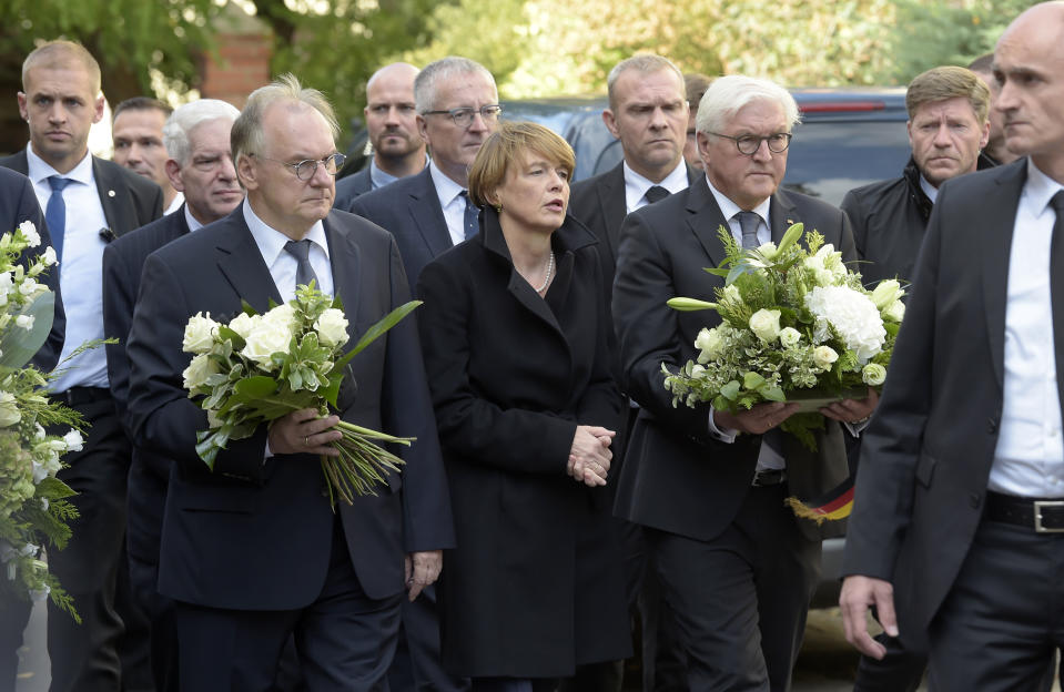 German President Frank-Walter Steinmeier, third right, holds a bunch of flowers as he and his wife Elke Buedenbender, center, arrive at a synagogue in Halle, Germany, Thursday, Oct. 10, 2019. A heavily armed assailant ranting about Jews tried to force his way into a synagogue in Germany on Yom Kippur, Judaism's holiest day, then shot two people to death nearby in an attack Wednesday that was livestreamed on a popular gaming site. (AP Photo/Jens Meyer)