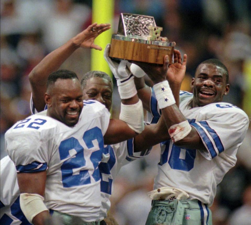 FILE - In this Sunday, Jan. 14, 1996 file photo, Dallas Cowboys’ Emmitt Smith (22) and Michael Irvin, right, hold up the NFC Championship trophy after the Cowboys defeated the Green Bay Packers 38-27 in Irving, Texas. The Dallas Cowboys and Green Bay Packers go way back _ as in the 1967 NFL Championship game played in such frigid conditions at Lambeau Field that it is known in league annals as the “Ice Bowl.” Cowboys. Packers. Fifty years of postseason history. While they may not be traditional rivals, their playoff meetings often leave an impression.(AP Photo/Eric Gay, File)